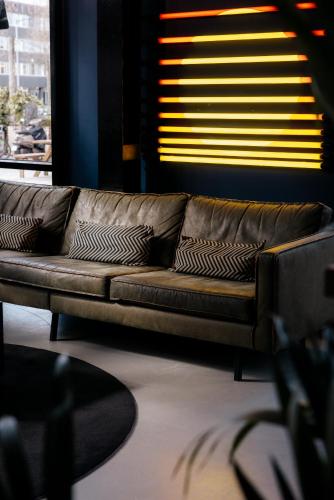 a brown leather couch in a room with a window at The Social Hub Amsterdam City Extended Stay in Amsterdam