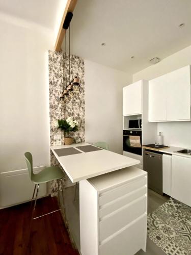 une cuisine avec des placards blancs et une chaise verte dans l'établissement Baiona Appart lumineux, à Bayonne