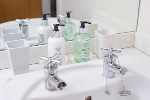 a bathroom sink with bottles of soap and a mirror at Gairn Apartment in Ballater