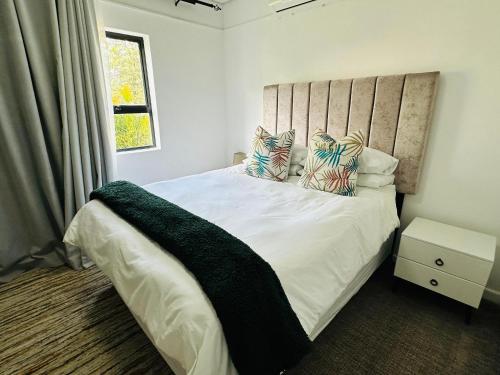 a bedroom with a white bed with pillows and a window at Cozy One-bedroom Apartment near GrandPalm Resort Block 5, Gaborone, Botswana in Mogoditshane