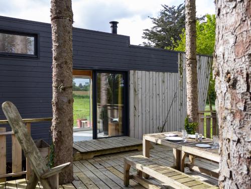 a black cottage with a wooden deck and a table at La Cafoutche Tiny - 5 personnes in Gommenecʼh