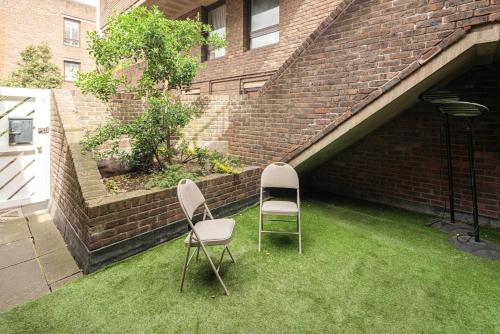 zwei Stühle auf dem Gras neben einer Ziegelmauer in der Unterkunft Stylish 3BD Flat in Prime Covent Garden Location in London