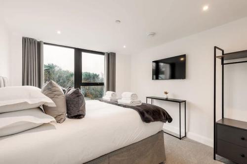 a white bedroom with a large bed and a television at Aurora South - Short Walk to Ashley Cross in Poole
