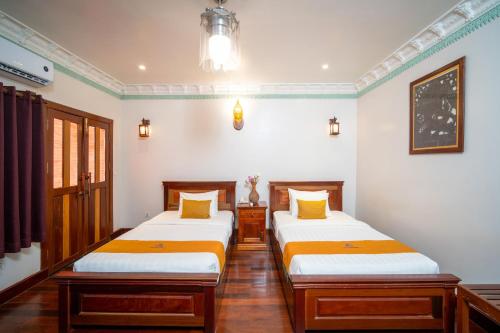 two beds in a room with white walls and wood floors at Hello Cambodia Hotel in Phumi Ta Phul