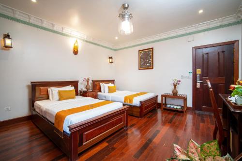 two beds in a room with wood floors and white walls at Hello Cambodia Hotel in Phumi Ta Phul