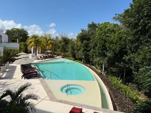 a large swimming pool with chairs and trees at Selva Tulum - HiveNB in Tulum