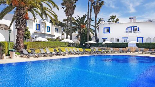 a pool with chairs and palm trees in front of a building at Pestana Palm Gardens in Carvoeiro