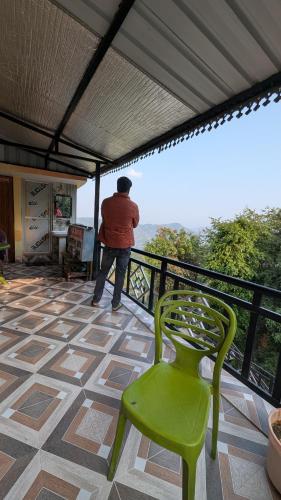 a man standing on a balcony with a green chair at Quarali Homestay in Mukteswar
