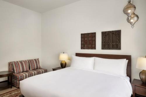 a bedroom with a large white bed and a chair at Aldhafra Desert Resort, Vignette Collection by IHG in Madīnat Zāyid