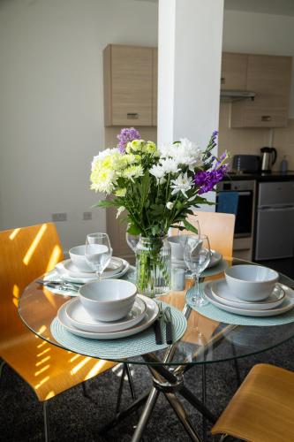a glass table with plates and a vase of flowers at The Trafford Luxe , Garage Parking, Self Check-in Anytime - Perfect for Late Arrivals, Ultra- Fast Wi-Fi, 5 mins to Old Trafford Stadium in Manchester