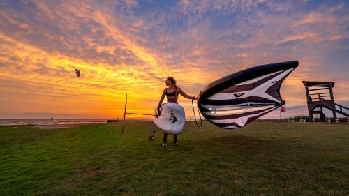 a woman standing on the beach holding a kite and a surfboard at Buxton Slick - Waterfront 2-Bedroom, 2-Bathroom Suite at REAL Watersports in Waves