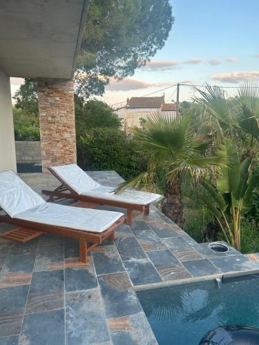 une terrasse avec deux chaises longues et une piscine dans l'établissement Villa Palmeraie 240m2 Piscine Jacuzzi, à Lieuran-lès-Béziers