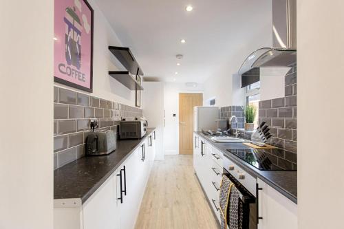 a kitchen with white cabinets and black counter tops at Cosy Cruise Cribs - SEAFORD in Stoke on Trent