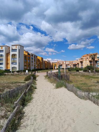 un chemin de sable devant des bâtiments sur une plage dans l'établissement Le Palm Beach vue mer le Barcares, au Barcarès