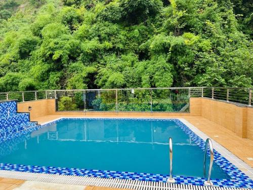 a swimming pool in front of a hill with trees at The Shri Shyam Prime Main Har Ki Pauri Haridwar in Haridwār