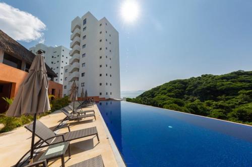 a pool with chairs and umbrellas next to a building at 3BR Sub-Penthouse With Ocean Views! in Cruz de Huanacaxtle