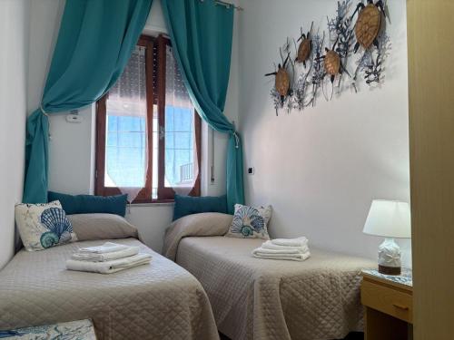 two beds in a room with blue curtains at all ombra dei pini in La Caletta