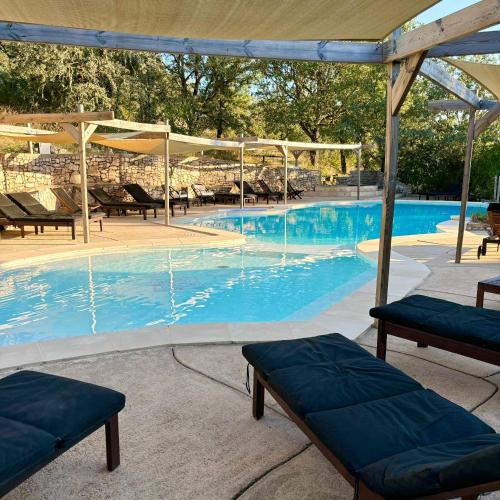 une grande piscine d'eau bleue et des bancs dans l'établissement Aux Lodges du Mas de Nadal, à Sauliac-sur-Célé