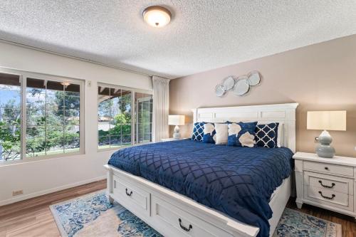 a bedroom with a bed with a blue comforter and two windows at Home in San Diego! The Blue Leaf with 3bed 2bath, Golf, Large Yard! in Rancho Bernardo