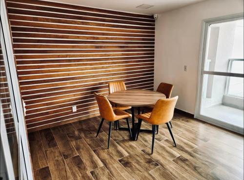 a table and chairs in a room with a wooden wall at Studio Novo Luxo - Centro in Mogi das Cruzes