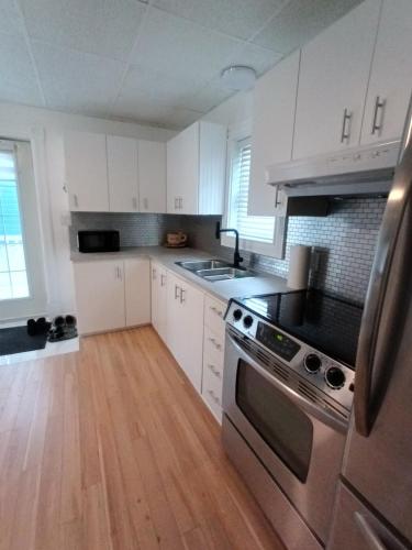 a kitchen with white cabinets and stainless steel appliances at Le Narval Hébergement Touristique in Saint-Siméon