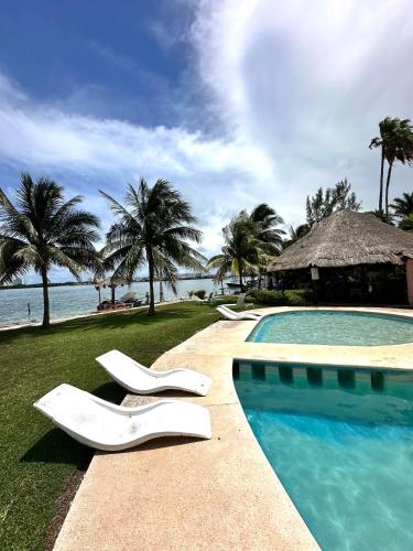 a swimming pool with white chairs next to the ocean at Hermoso departamento en zona hotelera frente a la laguna in Cancún