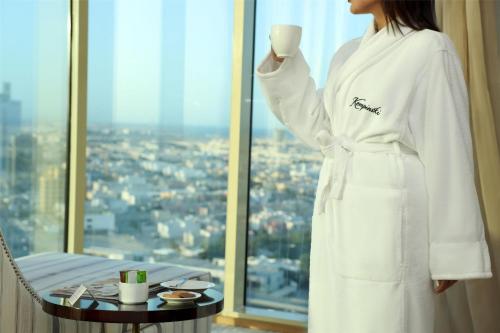 a woman in a white robe standing in front of a window at Kempinski Al Othman Hotel Al Khobar in Al Khobar