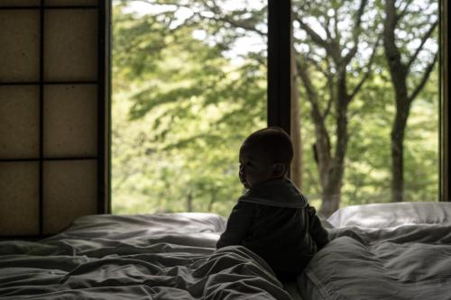 a child sitting on a bed looking out a window at FUMI hakone 森の露天風呂 in Hakone