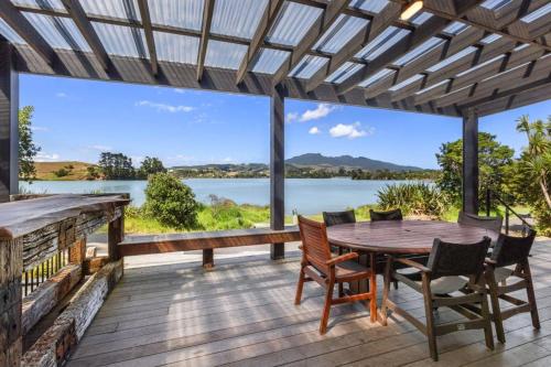 a wooden table and chairs on a deck with a view of a lake at Kaitoke Retreat and Studio, 10 guests, Waterfront in Raglan