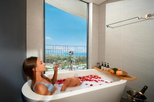 a woman sitting in a bath tub looking out the window at Wyndham Hoi An Royal Beachfront Resort & Villas in Hoi An