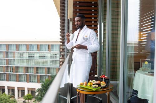 a man standing on a balcony with food on a table at Kempinski Hotel Gold Coast City in Accra