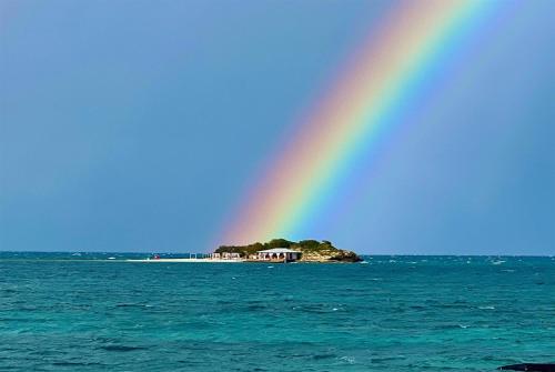 a rainbow in the sky over the water with a house at Hodges Bay Resort & Spa, an HQ Luxury Resort & Residences in Saint Johnʼs
