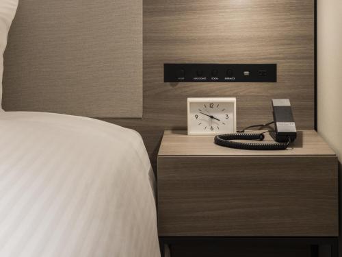 a bedroom with a bed and a clock and a phone at HOTEL FORZA SAPPORO STATION in Sapporo