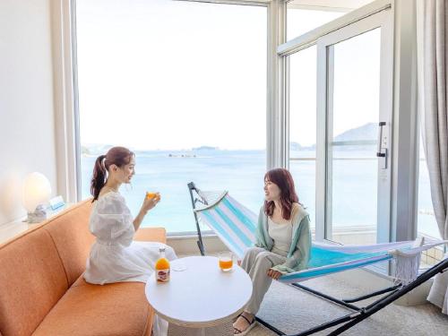 two women sitting in a hammock in a room with a table at Nichinankaigan Nango Prince Hotel in Nichinan
