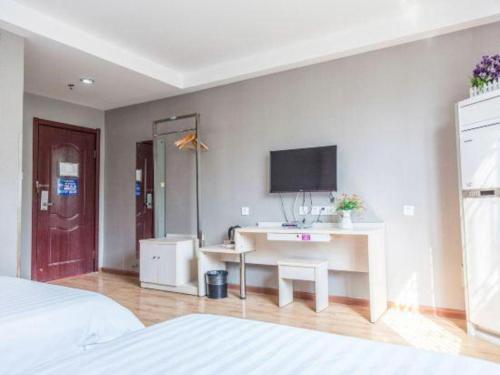 a bedroom with a desk and a tv on the wall at Kunlun Leju Business Hotel Kaifeng Gulou in Kaifeng