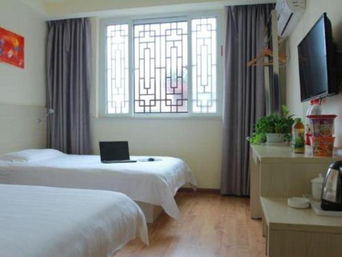 a bedroom with two beds and a laptop on the bed at Kunlun Leju Business Hotel Kaifeng Gulou in Kaifeng