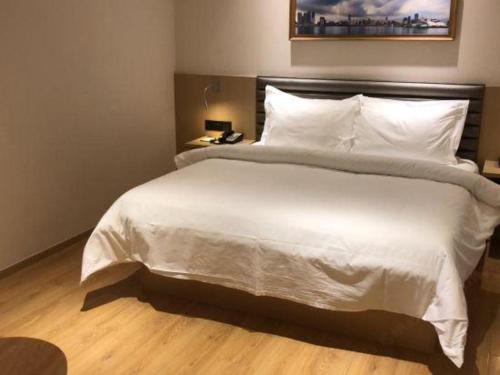 a bedroom with a large white bed with a telephone at Metropolo Hotel Qingdao Wusi Square Xiaomaidao in Qingdao