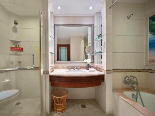 a bathroom with a sink and a tub and a mirror at Sanya Baohong Hotel in Sanya