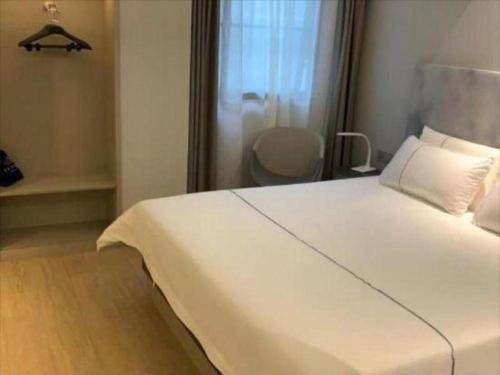 a large white bed in a room with a chair at Magnotel Shanghai Henglong Plaza in Shanghai