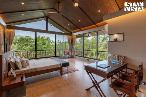 a bedroom with a bed and a desk and windows at Nivaant Farms by StayVista - Green Retreat with Pool, Orchard, Jacuzzi & Gazebo in Karjat