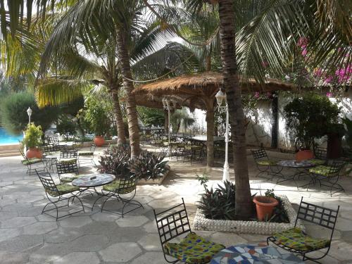 a patio with chairs and tables and palm trees at Hotel Club Safari in Mbour