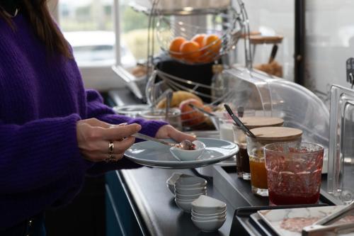 a woman eating a plate of food on a counter at The Originals Boutique, Hôtel Victoria, Châtelaillon-Plage in Châtelaillon-Plage