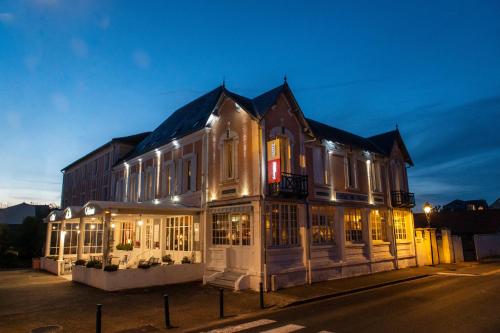 a large building with lit up windows at night at The Originals Boutique, Hôtel Victoria, Châtelaillon-Plage in Châtelaillon-Plage