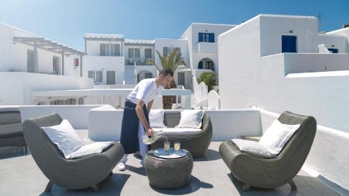 a man standing on a patio with chairs and a table at Lilly Residence-All Sea View Suites, Adults Only in Naousa