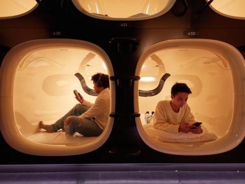 two men sitting in a room with their cell phones at Rembrandt Cabin Shinjuku Shin-Okubo in Tokyo