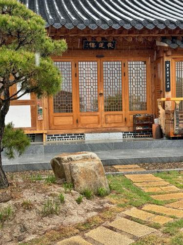 a building with a tree and a rock in front of it at Hanok Stay - JukRokJungSa in Gurye
