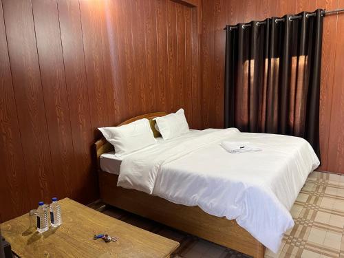 Un dormitorio con una cama con sábanas blancas y una mesa. en Bir Hotel by Aaroh, en Bīr