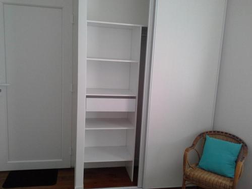 un placard avec des étagères blanches et une chaise avec un coussin bleu dans l'établissement Agréable studio à proximité du centre ville, à Tarbes