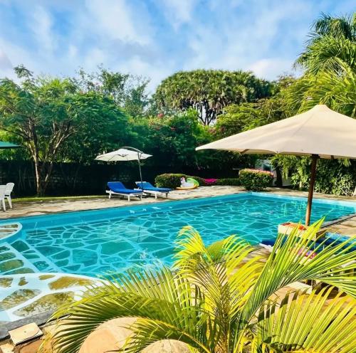 a swimming pool with an umbrella and chairs at WHITE Nyumba Malindi in Malindi