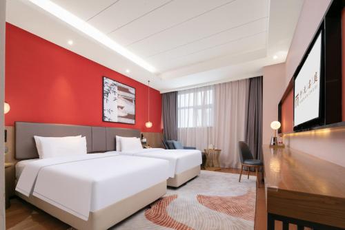 two beds in a hotel room with a red wall at Mansion New Century Hotel Chengdu Wuhou in Chengdu